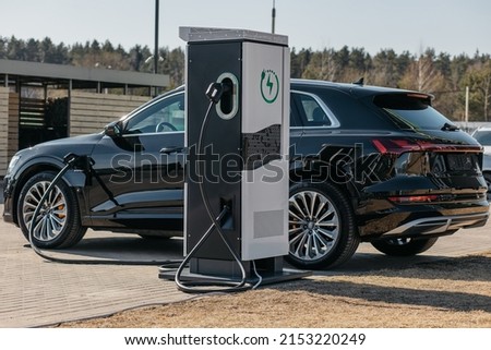 A photograph of an electric car being charged from a portable electric vehicle charging station located right in a parking lot in the city. Royalty-Free Stock Photo #2153220249