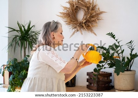 Elderly woman watering indoor plants from a watering can Royalty-Free Stock Photo #2153223387
