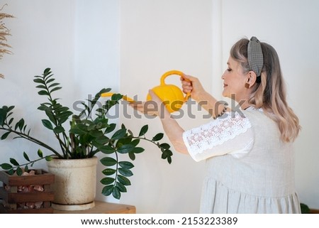 Elderly woman watering indoor plants from a watering can Royalty-Free Stock Photo #2153223389