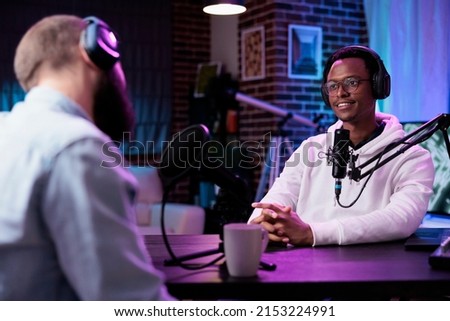 Podcast presenter having live conversation with young man, recording discussion for audience on internet channel. Male influencer enjoying chat with guest, broadcasting with production equipment.