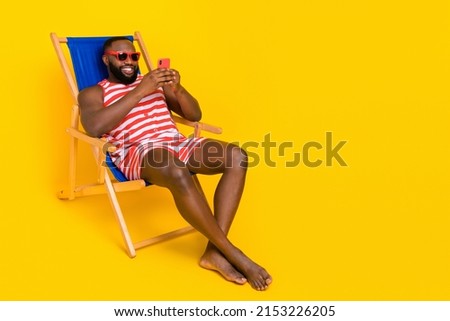 Photo guy student sit deckchair use device relax wear barefoot swim suit shorts isolated bright color background