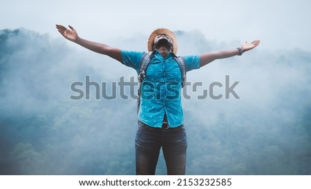 Freedom african traveler man carrying a backpack stands at the top of a mountain on a foggy day.Adventure travel and success concept Royalty-Free Stock Photo #2153232585