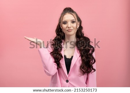 The shocked woman looks to the side points hand she is excited surprised. Elegant young girl on pink background.