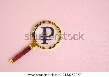 Ruble symbol under magnifying glass, on pink background