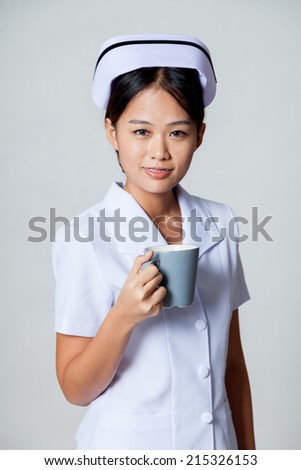 Young Asian nurse with a cup of coffee on gray background