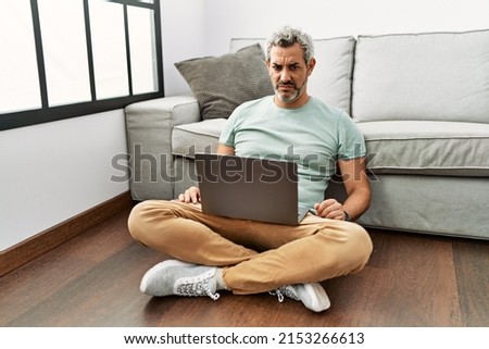 Middle age hispanic man using laptop sitting on the floor at the living room skeptic and nervous, frowning upset because of problem. negative person. 