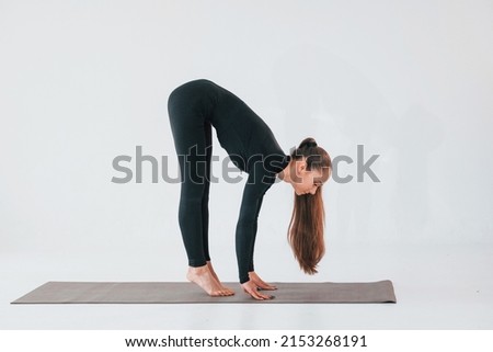 Side view. Young woman in sportive clothes doing gymnastics indoors.