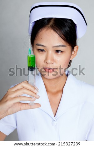 Young Asian nurse look at syringe with green medicine on gray background
