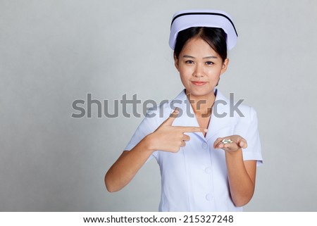 Young Asian nurse point to pills on her palm hand on gray background