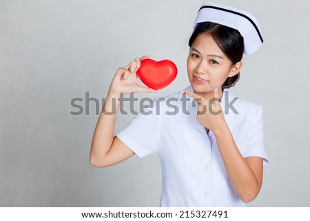 Young Asian nurse point to red heart on gray background
