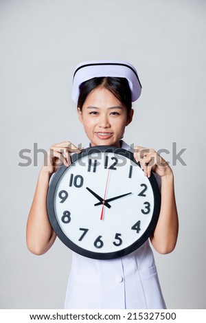 Happy time of  young Asian nurse with a clock on gray background