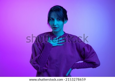 Looks astonished. Portrait of young charming girl, student posing isolated over purple studio background in neon light. Concept of youth, fashion, emotions, vision and facial expression.