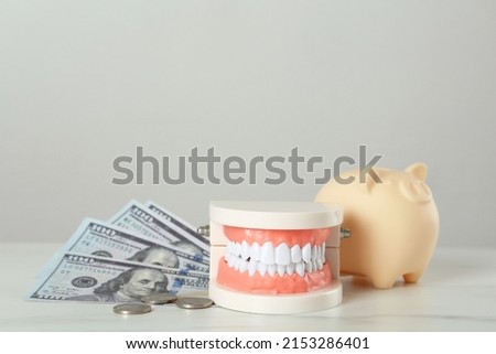 Educational dental typodont model, piggy bank and money on white table. Expensive treatment