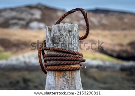 Closeup photo of an old brown rusty metal rope wound around an old decaying wooden anchor post used to dock ships in the harbour.