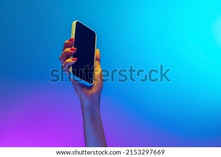 News. Closeup female hands holding gadget, smartphone isolated on gradient blue and purple background in neon. Concept of mobile lifestyle, digital technology, social gathering. Royalty-Free Stock Photo #2153297669