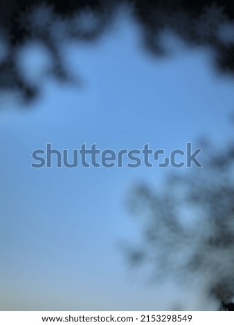 Defocused or blurred abstract background of a flying traditional balinese kite in the blue sky and flanked by two branches of tree
