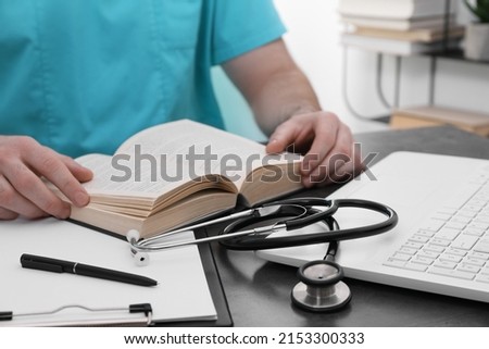 Medical student in uniform studying at table indoors, closeup Royalty-Free Stock Photo #2153300333