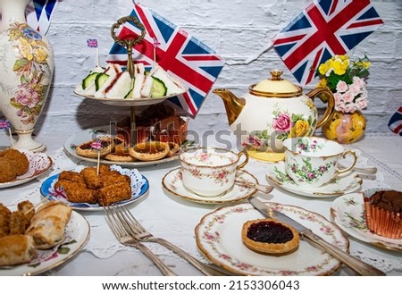 Queen Elizabeth II Platinum Jubilee cream tea street party food red white and blue flags  with celebration Union jack food toppers on a white vintage table cloth with Union jack flags Royalty-Free Stock Photo #2153306043