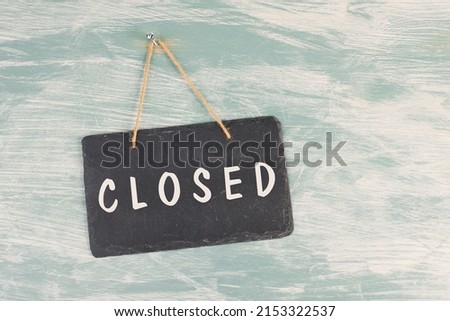 The word closed is standing on a chalkboard sign, hanging on a blue textured weathered door, concept for business, stores and restaurants