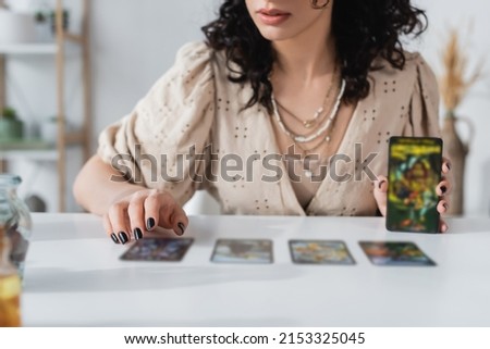 Cropped view of soothsayer holding blurred tarot cards near table Royalty-Free Stock Photo #2153325045