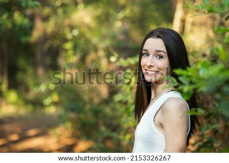 A beautiful happy teenage brunette girl outdoors in a wooded area in the spring with copy space.
