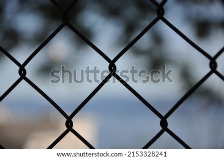 An abstract patterend shot of wire mesh fencing with blurred colorful city in the background.Abstract wire metal fence with blurry background. A fence or cage made with wire metal for protection.