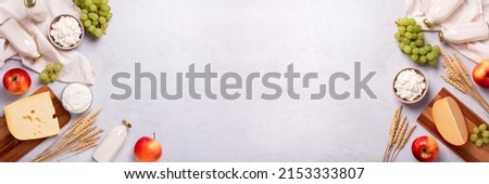 Shavuot flat lay with dairy products, first fruits and wheat on light gray background, web banner. Jewish Shavuot holiday frame with dairy foods and fruits, top view Royalty-Free Stock Photo #2153333807