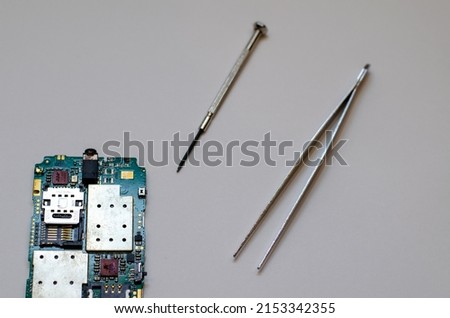 Disassembled mobile phone on the table of a mechanical engineer during repair. Tweezers and screwdriver for repairing electronic gadgets on a white background.