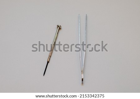 Tweezers and screwdriver for repairing electronic gadgets on a white background. The desktop of a mechanical engineer