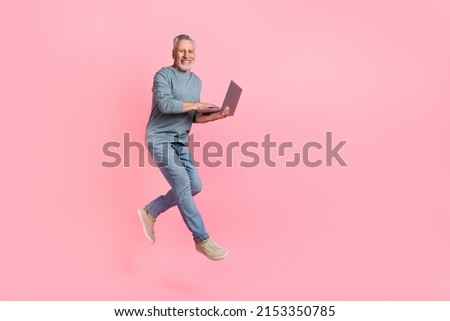 Photo of cute man pensioner dressed grey shirt jumping typing modern device empty space isolated pink color background