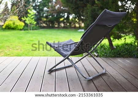 Folding chair surrounded by green leaves on a wooden deck. Relaxation in the garden. Cottage aesthetics. Vacation outside the city. Warm summer day. terrace Royalty-Free Stock Photo #2153361035