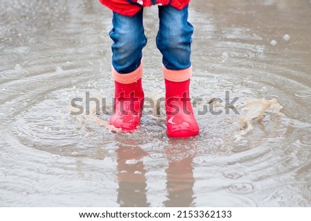 A cute little girl red boots jump in puddles and has a fun. Happy childhood. Early spring. Emotions.