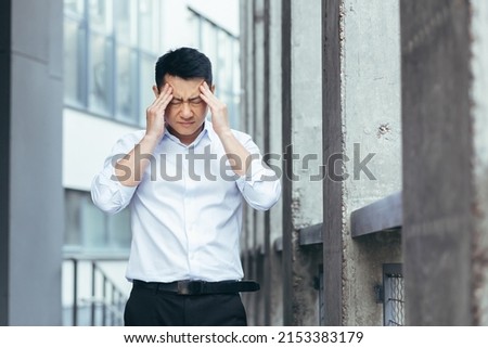 Tired and sad Asian has a severe headache, a businessman outside the office, holding hands behind his head Royalty-Free Stock Photo #2153383179