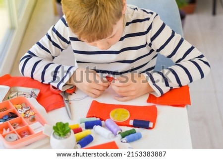 Close-up of a beautiful 9-year-old Caucasian boy who studies to sew with a needle and thread. Royalty-Free Stock Photo #2153383887