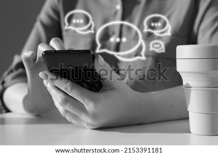 Woman using phone for sending messages. Online social communication concept. Female sitting at table with takeaway cup and chatting, sharing information. Black and white. High quality photo
