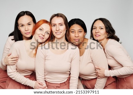 Portrait of content pretty multi-ethnic women hugging together while posing against white background, international womens friendship concept Royalty-Free Stock Photo #2153397911