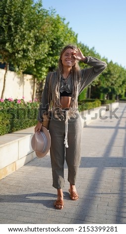 Portrait of a smiling girl with dreadlocks. Bohemian woman in boho style holding a hat. A charming girl with freckles in a hat smiles and laughs merrily. Bright and beautiful smile, street style.