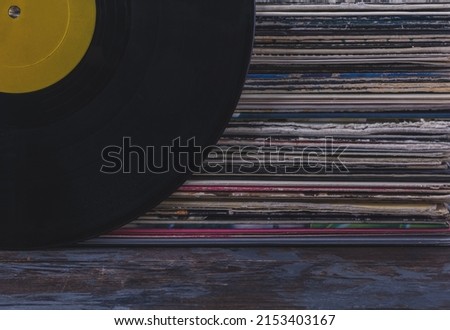 A stack of old vinyl records stacked on top of each other in multi-colored covers, on the side is a black vinyl record with a yellow blank label for text. Jazz vinyl record listening concept. Royalty-Free Stock Photo #2153403167