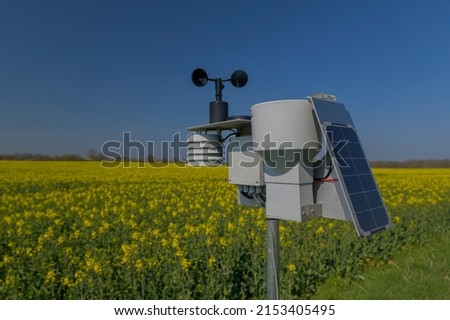 Smart agriculture and smart farm technology. Meteorological instrument used to measure the wind speed and solar cell system in the raps field. Weather station with solar panel placed in the field. Royalty-Free Stock Photo #2153405495