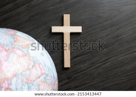 Christian cross on a dark wood background with a partial border of a world globe
