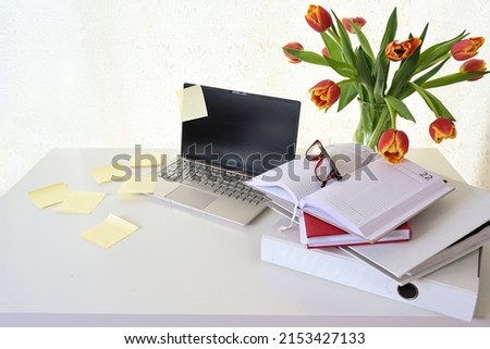 Laptop with a lot of sticky notes, ring binder, organizer and a bouquet of tulips on a white desk, concept for stress in home office, business or study, copy space, selected focus, narrow depth of fie