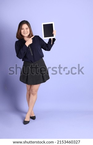 The chubby Asian woman standing on the purple background with the casual clothes.