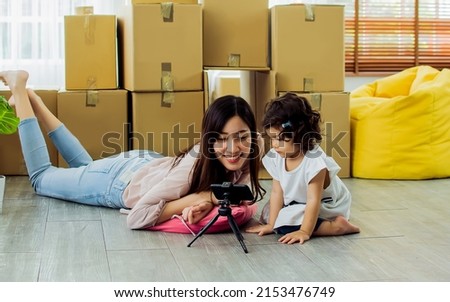 Asian adult happy beautiful mother playing, smiling using camera to take selfie photo with her little cute adorable mixed race daughter in comfortable house while moving new home. Family Concept