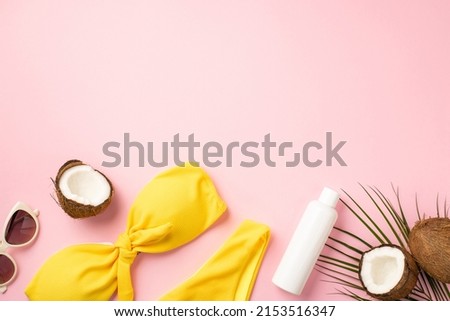 Summer holidays concept. Top view photo of sunglasses yellow bikini sunscreen tube cracked coconuts and palm leaves on isolated pastel pink background with empty space