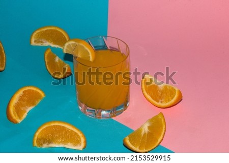 orange juice with lots of slice orange around glass on a pink-blue background and copy space