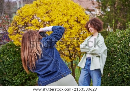Young model posing for professional photographer on flower street landscape. Woman hold digital camera in her hands.