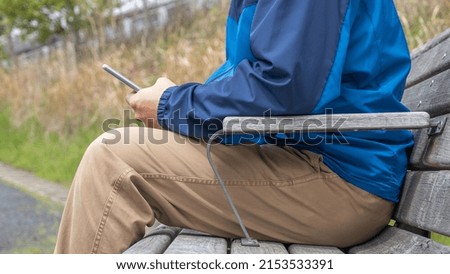 A man sitting on a park bench. He uses a smartphone.