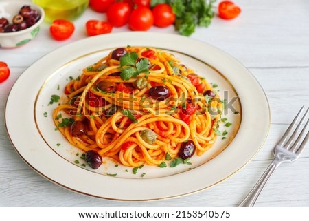 Italian Traditional Dish"Spaghetti alla Puttanesca",spaghetti with tomato sauce,anchovy,capers,olives,olive oil,peppers and parleys on plate with white wood table background.Simple and easy recipe Royalty-Free Stock Photo #2153540575