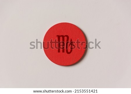 shot of a red wooden circle on a white background with a zodiac sign engraved on it, specifically the Scorpio sign