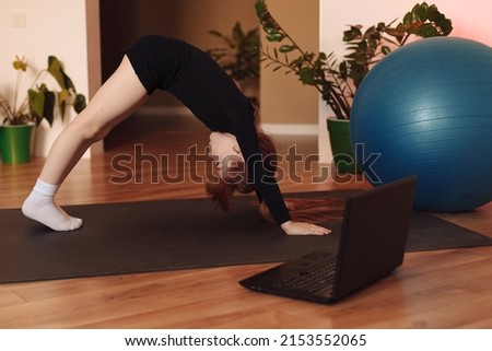  the girl sits in front of the laptop on the sports mat and repeats the exercises in stretching. 